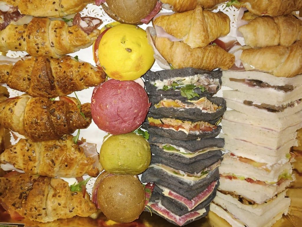 Una bandeja con filas de cruasanes salados, panecillos de colores y tramezzini blancos y negros